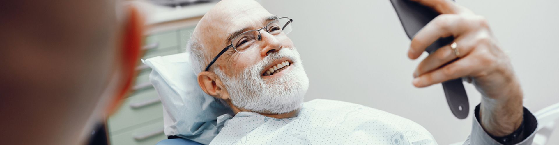 man admiring smile in hand mirror in dental chair