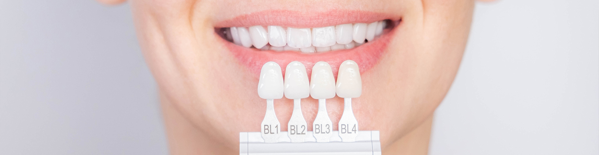 woman holding shades of veneers next to her teeth