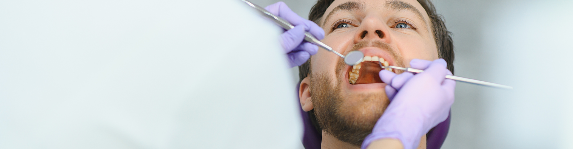 dentist holding dental tools in man's open mouth