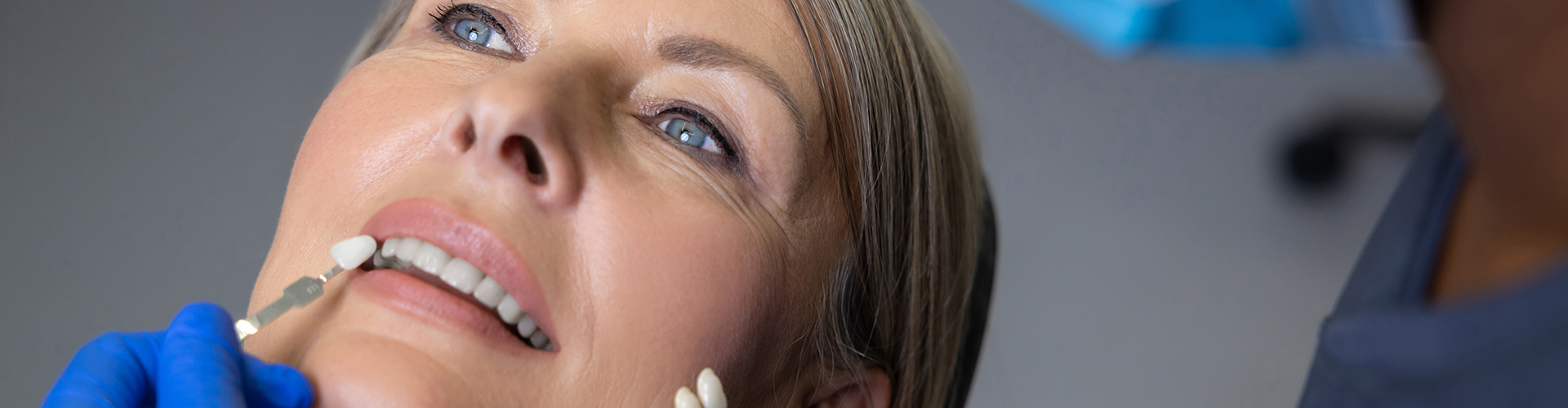 gloved hands holding color-matching tool against woman's teeth