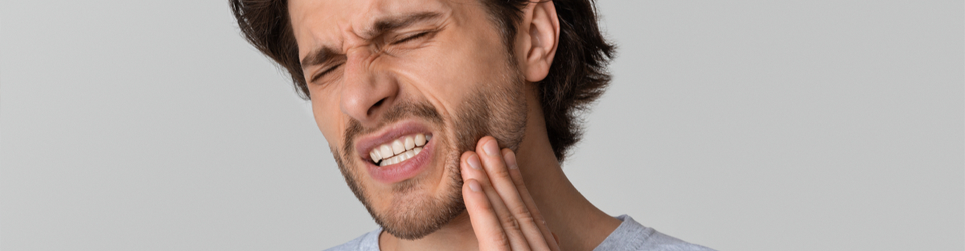 man holding side of his face clenching his teeth 