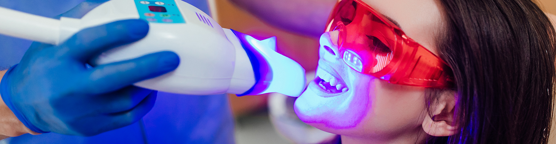 woman having LED light shined on her teeth by dentist