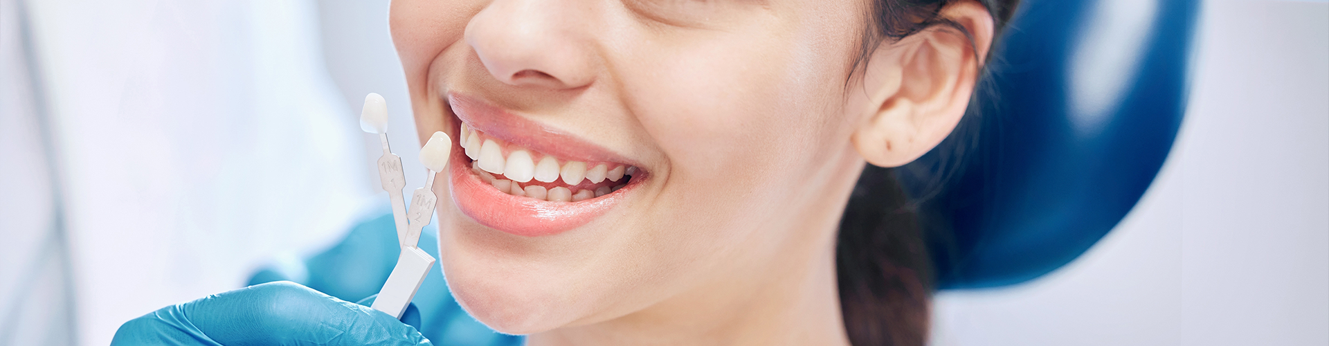 gloved hand holding shade-matching tool next to woman's smile