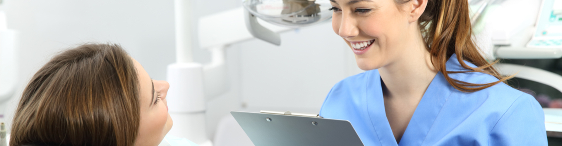 dental assistant with clip board smiling at patient 