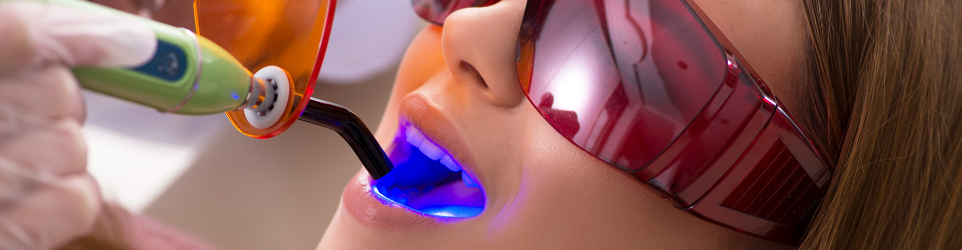 led light shining in the mouth of woman wearing eye protection