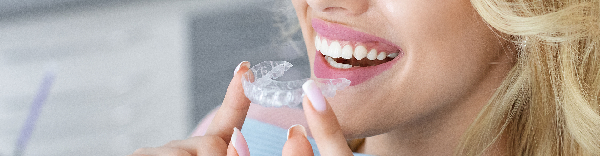 smiling woman holding Invisalign aligner in front of her mouth