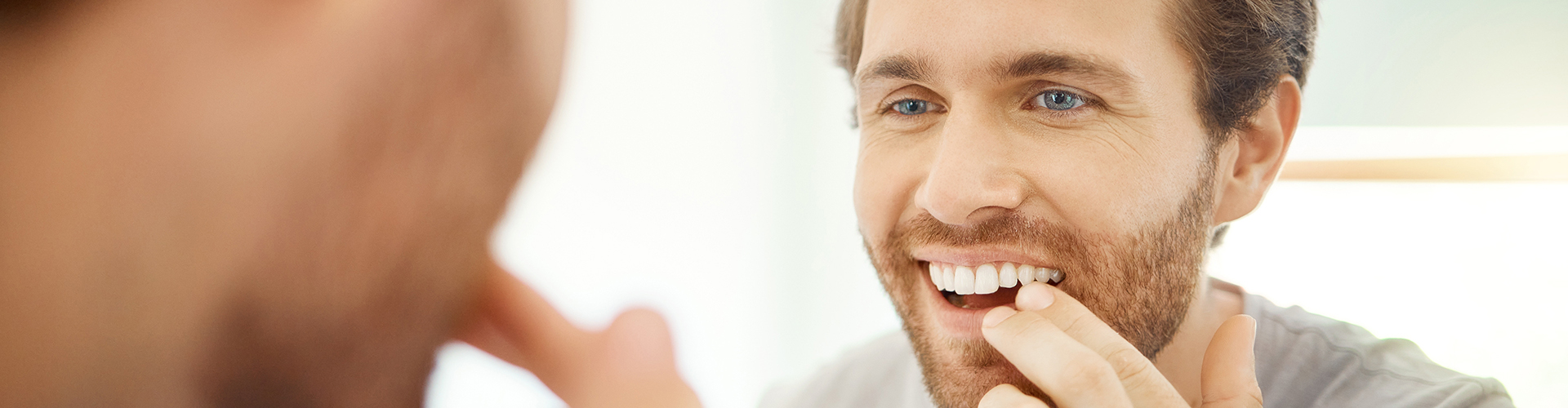 man smiling into mirror touching his teeth