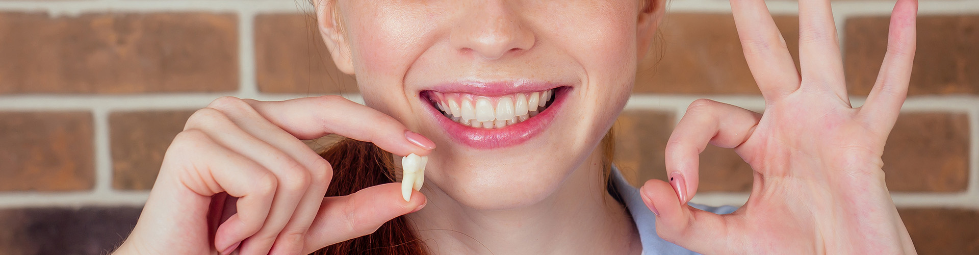 female smiling with a tooth in one hand making the okay sign with the other