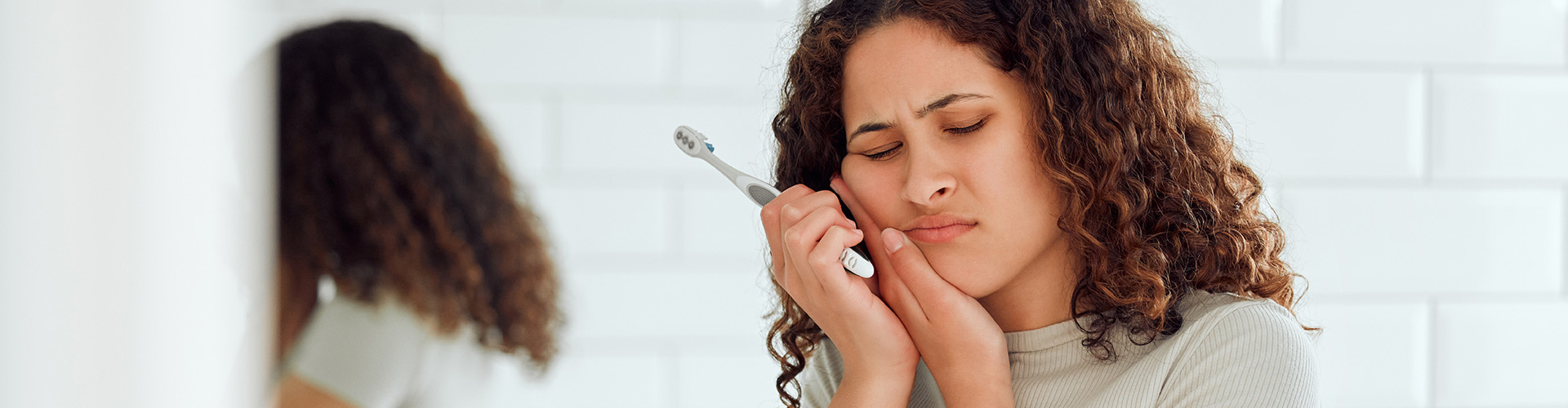 woman with toothbrush holding cheek in pain