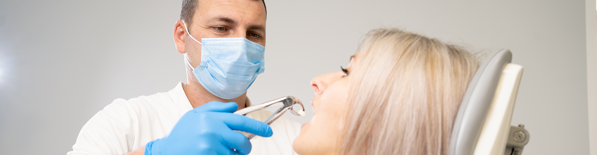 dentist holding tooth in pliers at woman's mouth