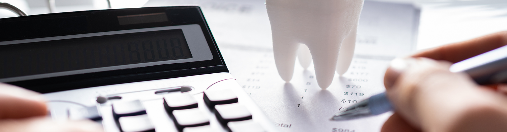 calculator and a model tooth on paperwork with hands holding an ink pen
