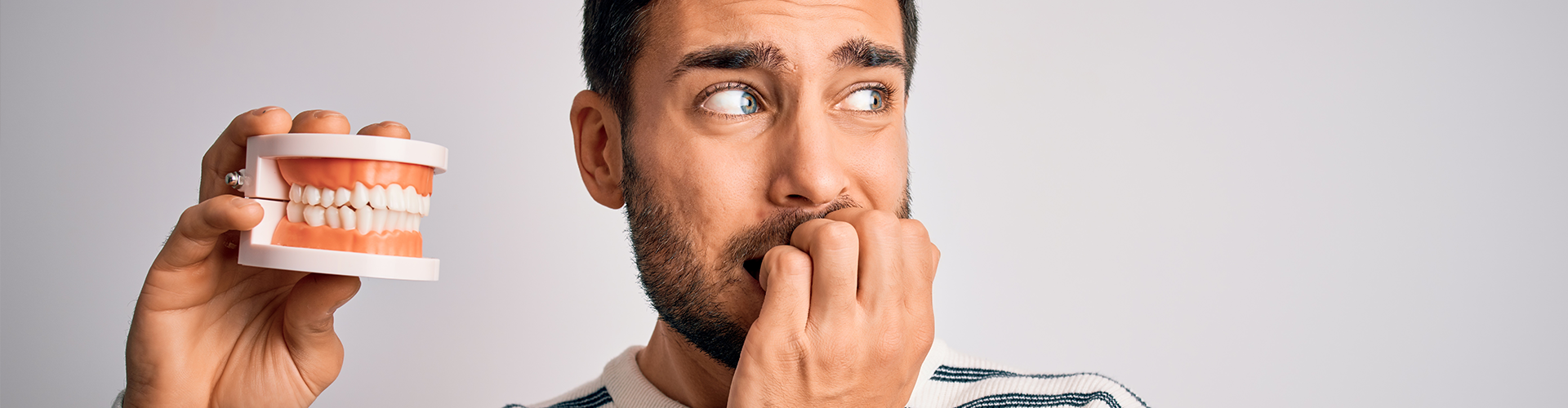 man holding teeth model while nervously biting his nails