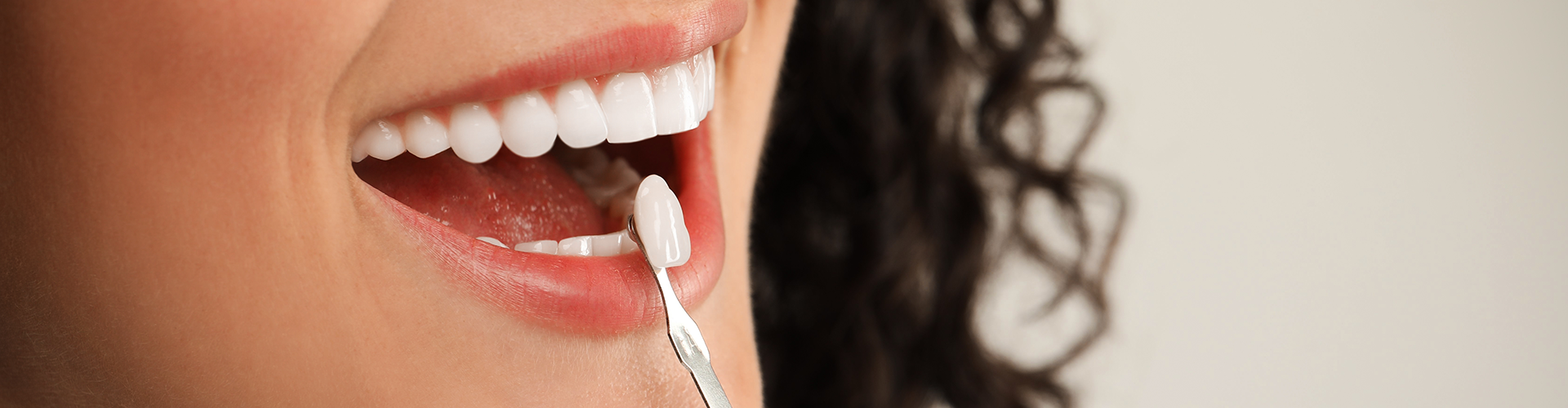 gloved hands holding tooth shade-matching tool against woman's smile